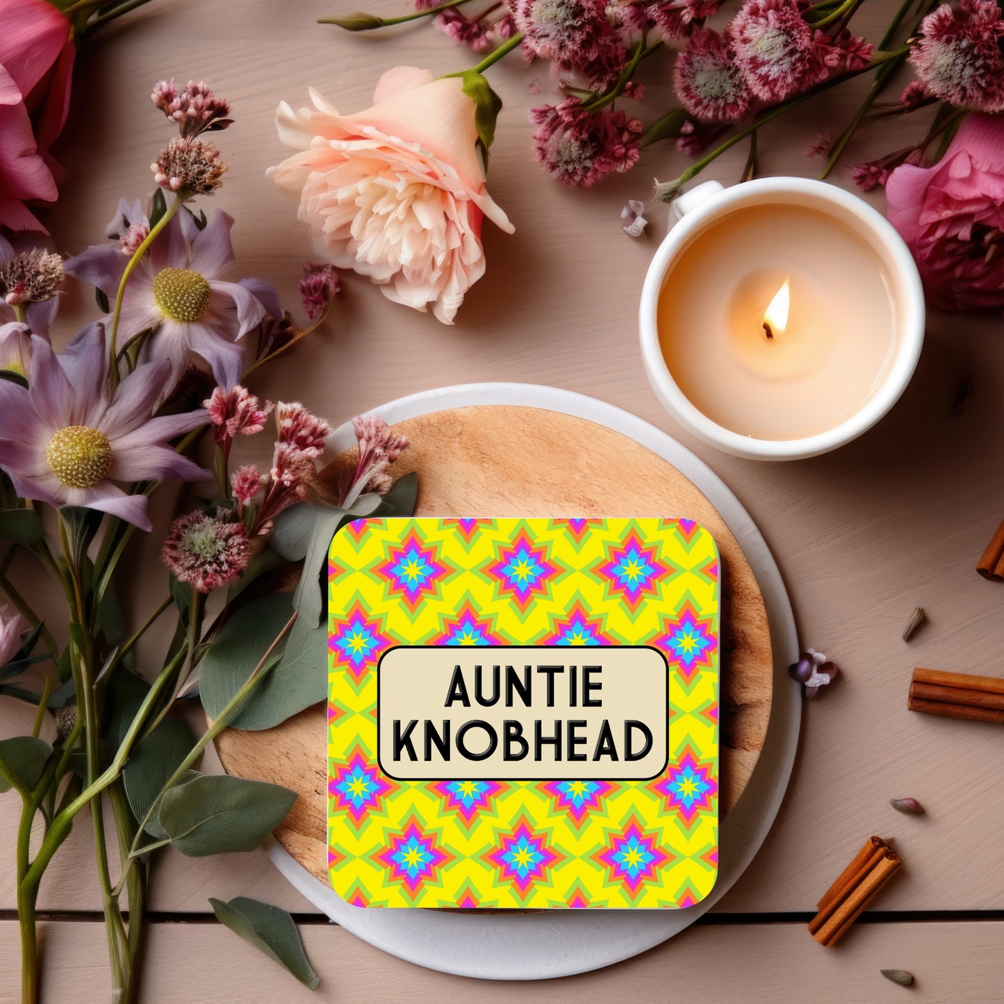 A square coaster with a colorful geometric pattern and the text 'AUNTIE KNOBHEAD' in bold letters.