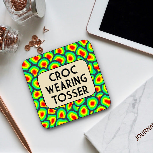 Colorful coaster with 'Croc Wearing Tosser' text on a white surface with stationery items.