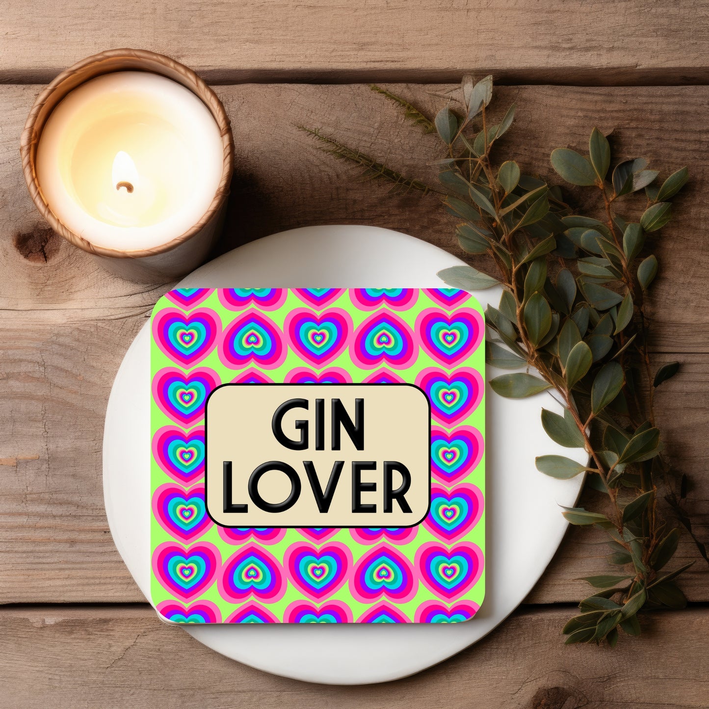 Coaster with 'Gin Lover' text on a colorful heart pattern, placed on a wooden surface with a candle and leaves.