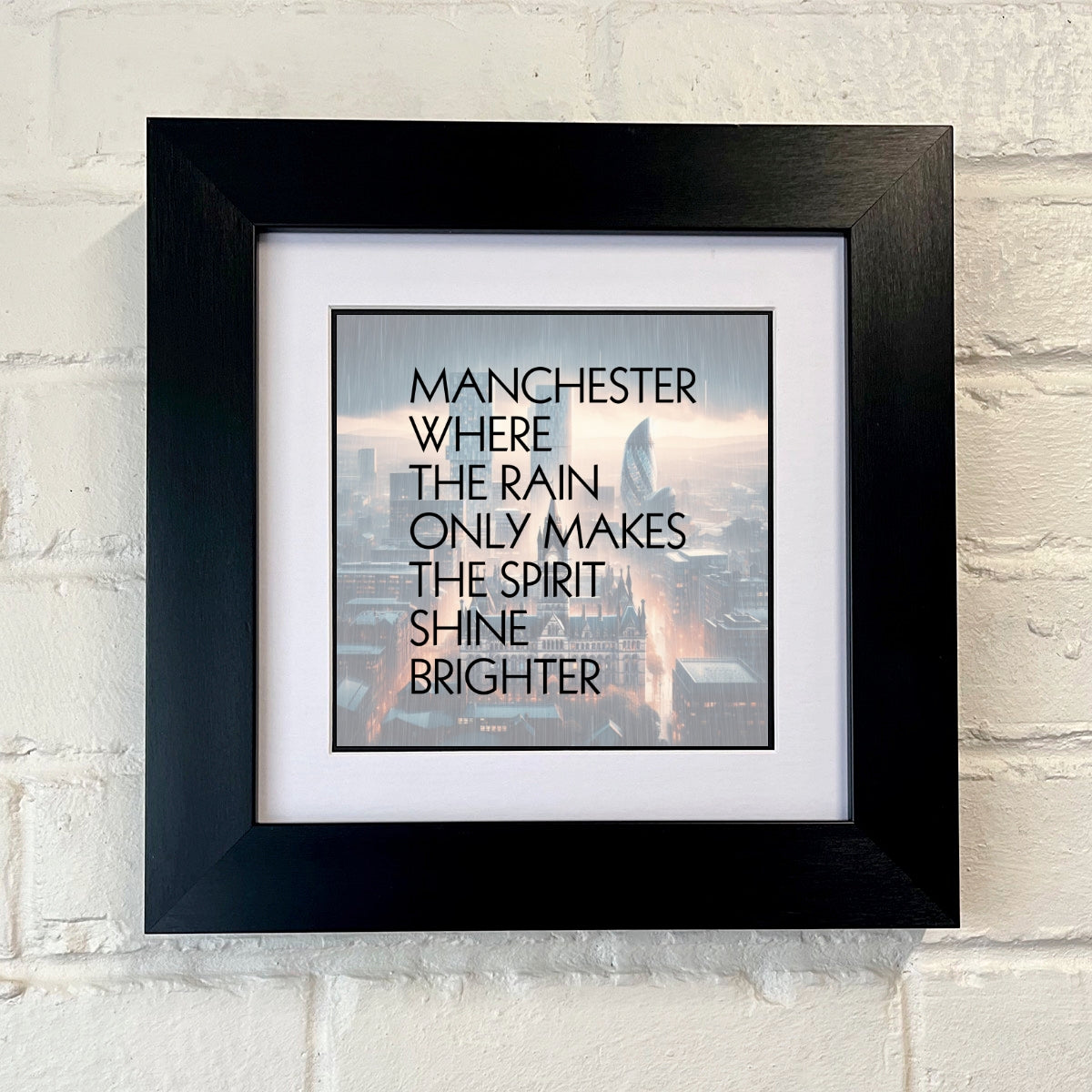 A FRAMED print with the text 'MANCHESTER WHERE THE RAIN ONLY MAKES THE SPIRIT SHINE BRIGHTER', featuring an image of a cityscape in the background.SU MACE GIFTS