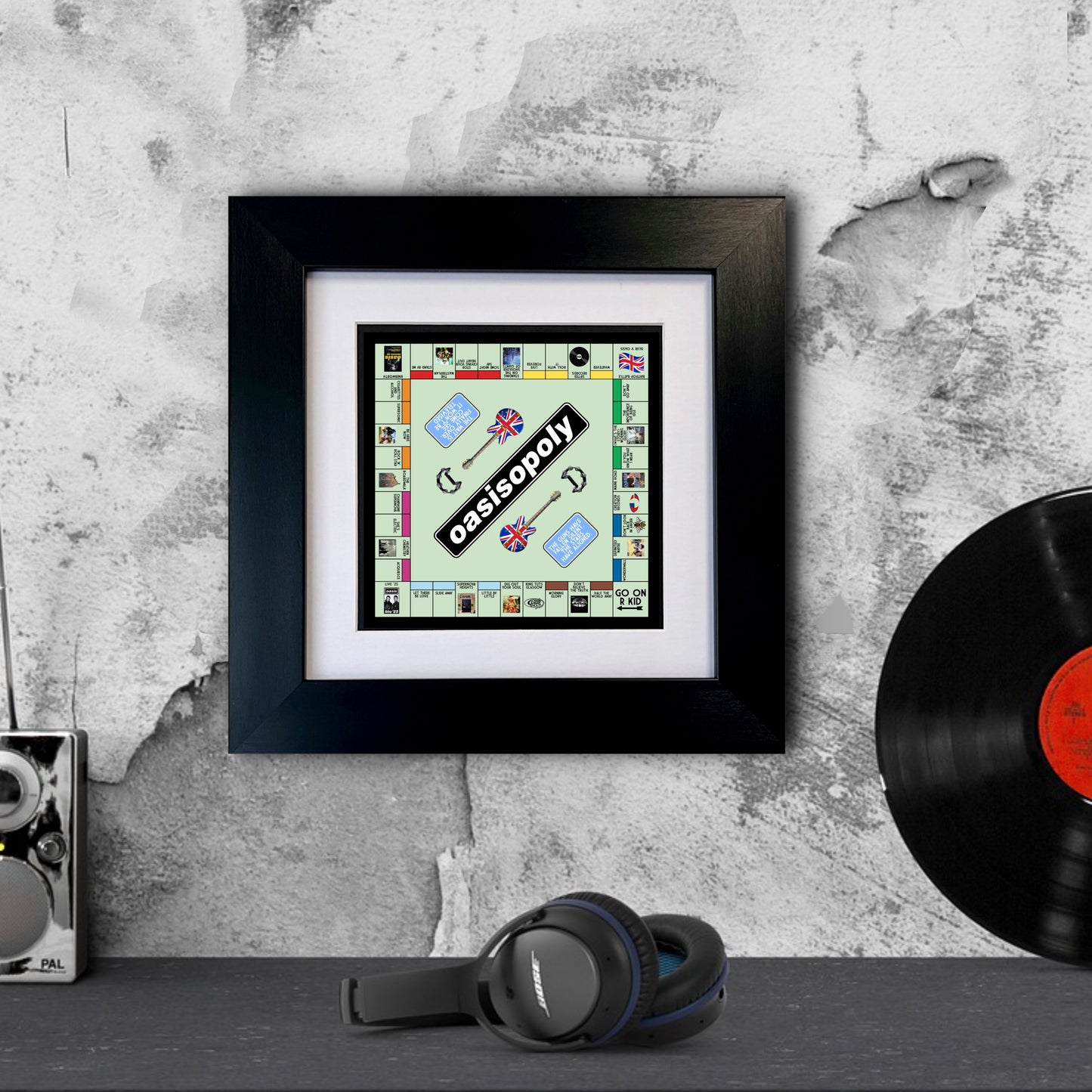 Framed Oasis monopoly board game piece on a textured wall with headphones and vinyl record.