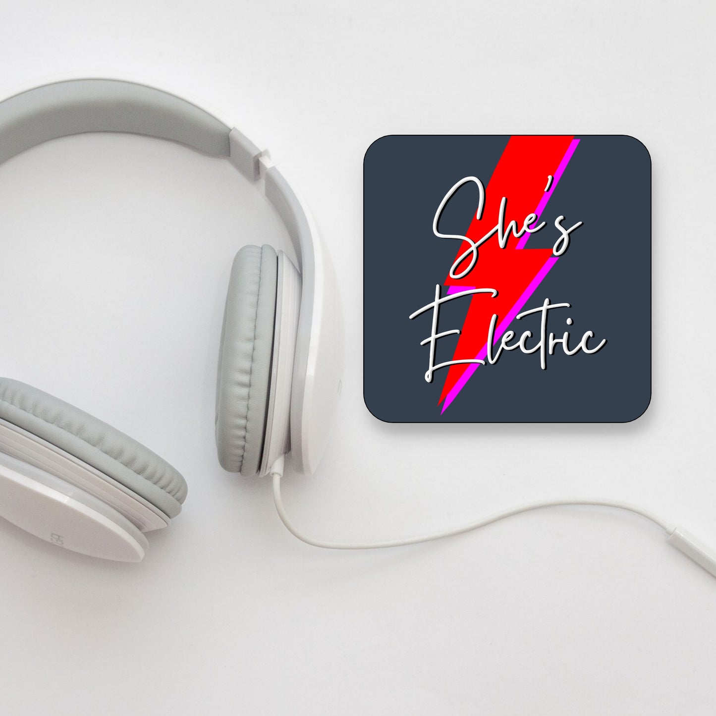 A square coaster with a gloss finish, featuring the text 'She's Electric' with a red lightning bolt design on a dark background. OASIS LYRICS