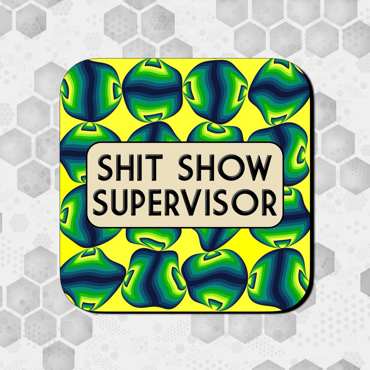Coaster with a bold yellow background covered in abstract green and blue geometric shapes, featuring a rounded beige box in the center with bold black text reading ‘Shit Show Supervisor.