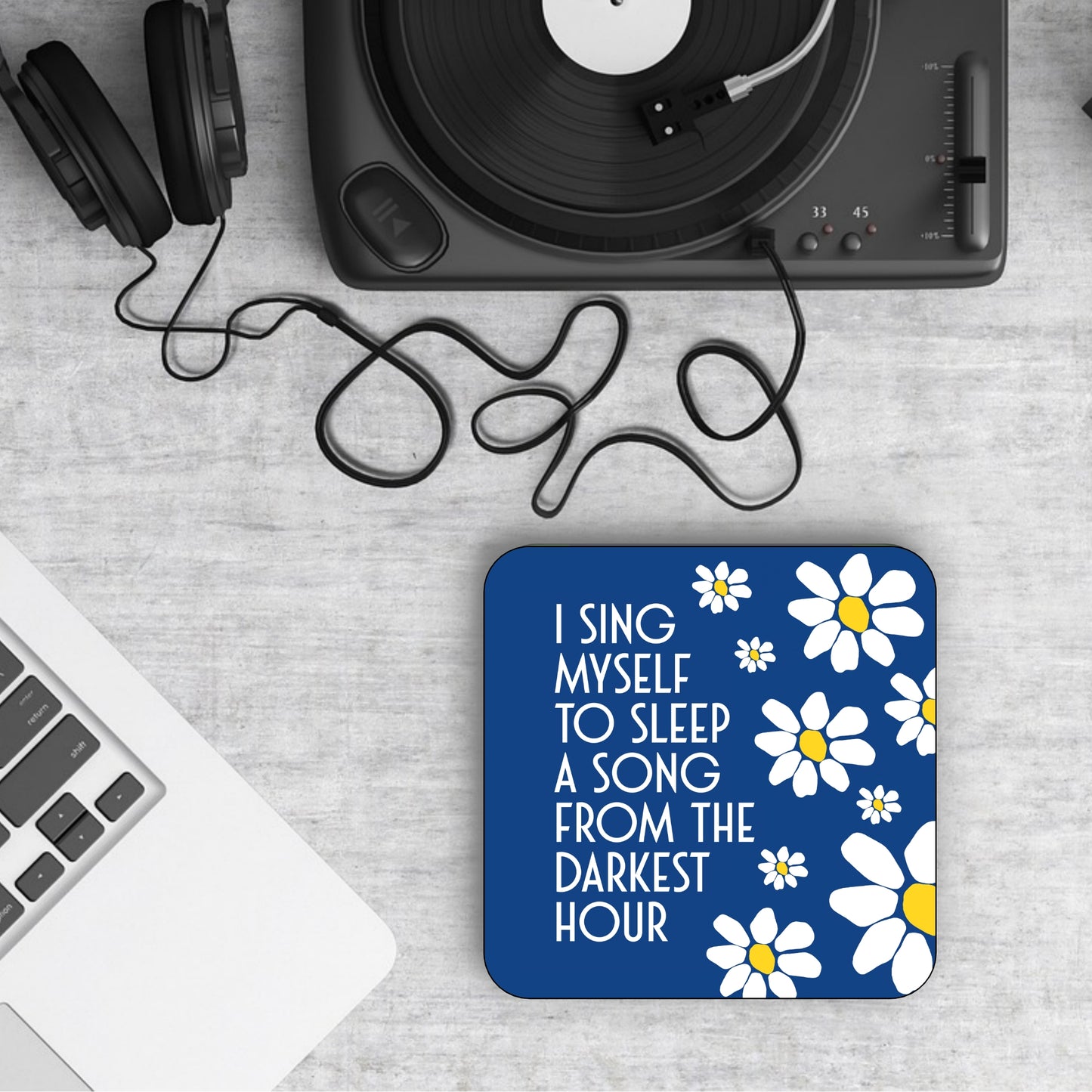A square coaster with a blue background featuring white flowers and the text 'I SING MYSELF TO SLEEP A SONG FROM THE DARKEST HOUR'. JAMES LYRICS