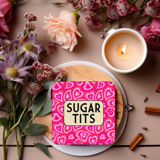 Coaster with a bright pink heart-patterned background, featuring a rounded beige box in the center with bold black text reading ‘Sugar Tits