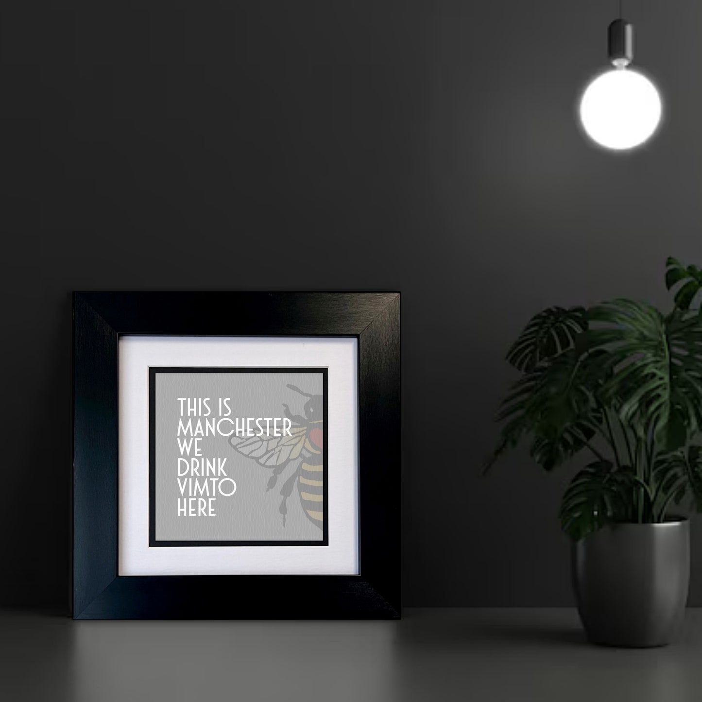 Framed print with 'This is Manchester, we drink Vimto here' text on a GREY BACKGROUND WITH A MANCHESTER BEE
