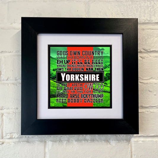 A framed print with a black frame displaying a colorful text-based artwork related to Yorkshire sayings.