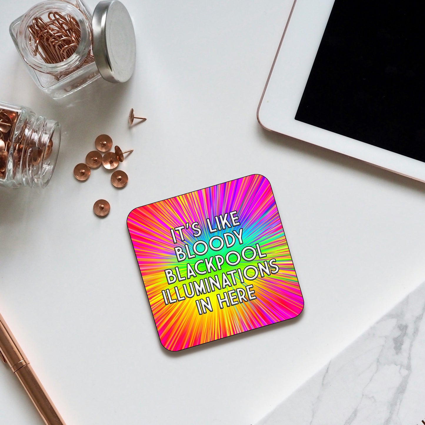 Coaster with a bright rainbow burst background radiating from the center, featuring bold text that reads ‘It’s like bloody Blackpool illuminations in here