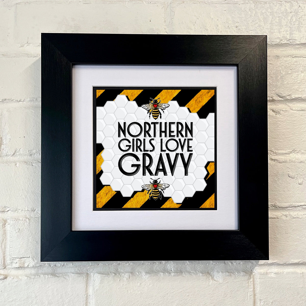 A framed print with the text 'NORTHERN GIRLS LOVE GRAVY' displayed on a BLACK AND YELLOW STRIPE  background with a graphic of a bee to the right side.