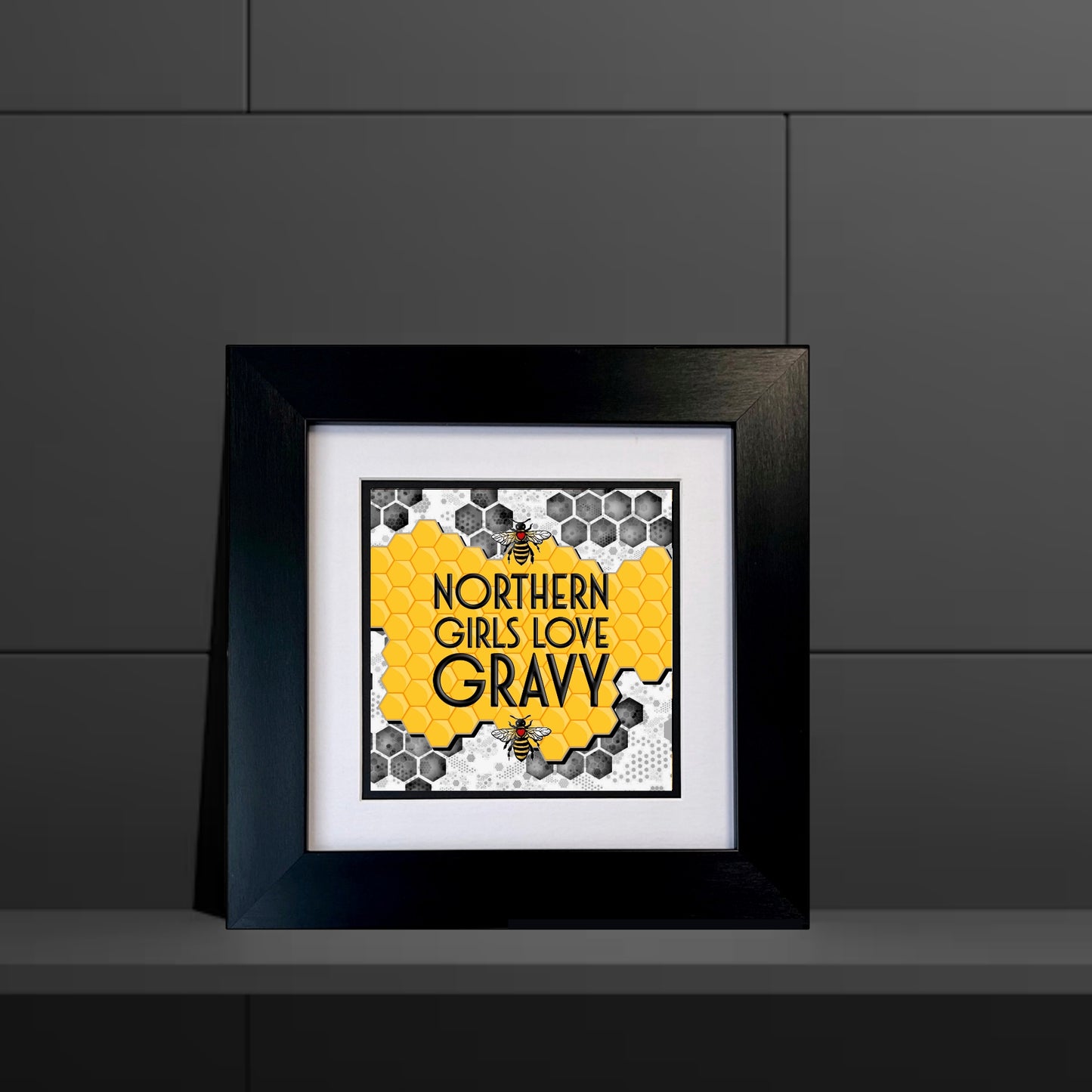 Framed artwork with 'Northern Girls Love Gravy' text on a honeycomb pattern against a dark gray background.