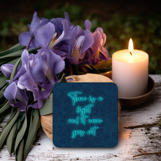 A square coaster with a blue background featuring the text 'There is a light and it never goes out' in a BRIGHT BLUE font. THE SMITHS LYRICS