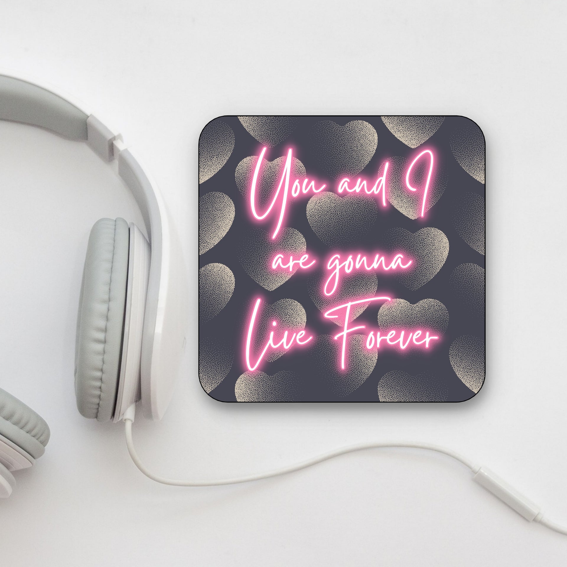 A square coaster with a dark background and pink text that reads 'You and I are gonna Live Forever', with a heart pattern in the design. OASIS LYRICS