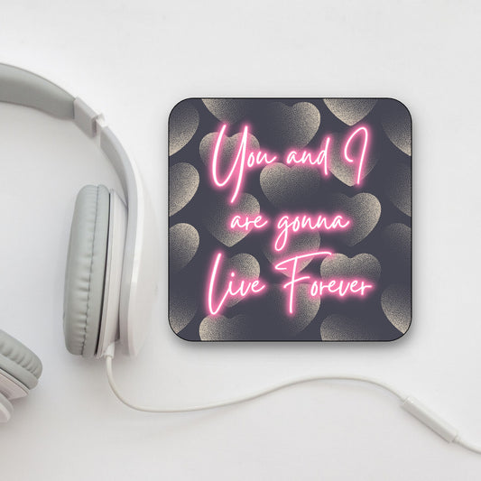 A square coaster with a dark background and pink text that reads 'You and I are gonna Live Forever', with a heart pattern in the design. OASIS LYRICS