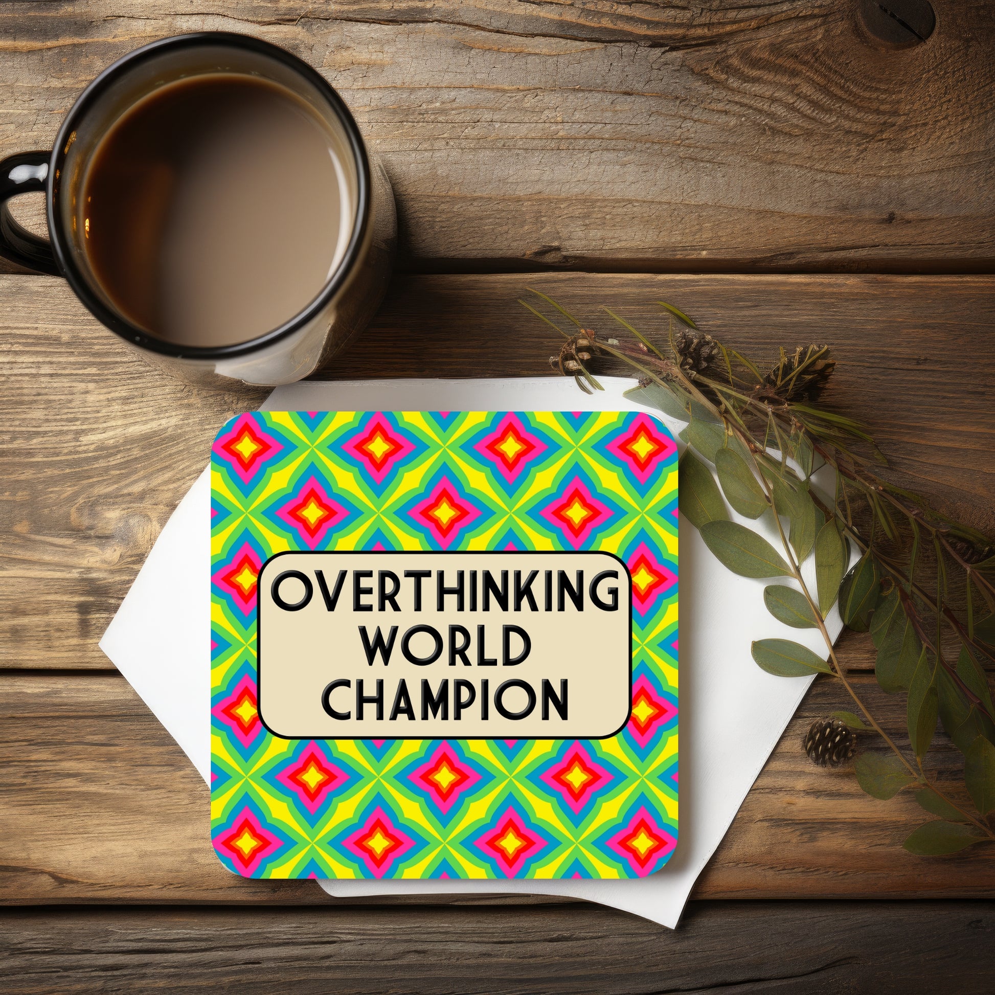 Colorful card with 'Overthinking World Champion' text on a wooden surface with a mug and leaves.