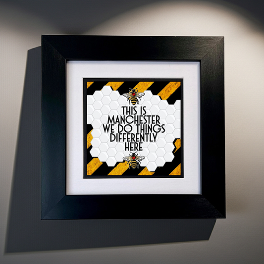 Framed artwork with Manchester bee design and text on a gray background