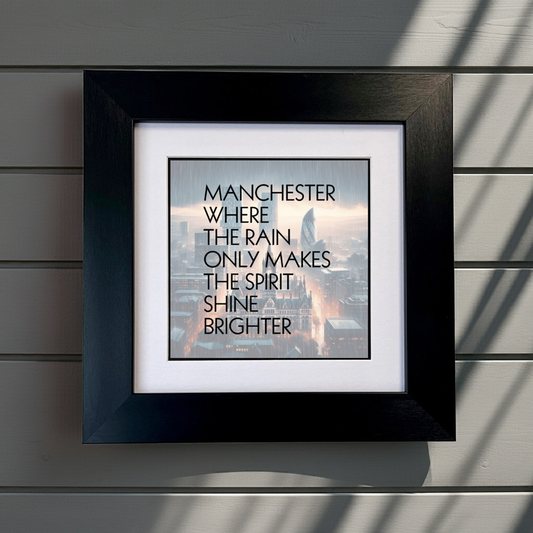 Framed print with text 'Manchester where the rain only makes the spirit shine brighter' on a wooden surface. SU MACE GIFTS